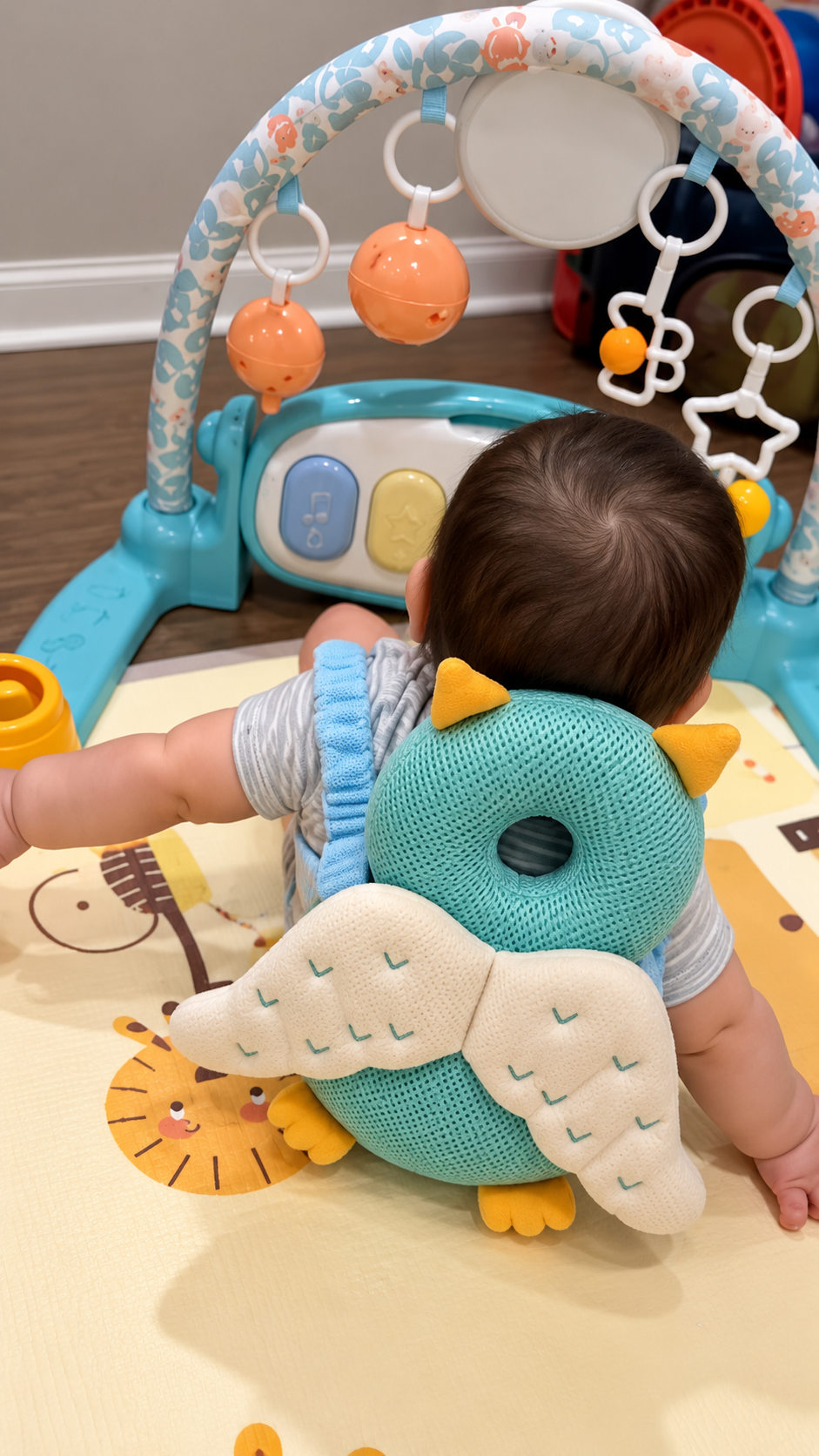 Baby sitting on a play mat wearing an owl plush backpack